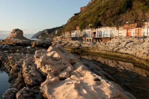 Scogliere rocciose e cabine colorate sulla spiaggia del Passetto, illuminate dalla luce dorata del tramonto.