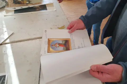 Hände halten ein Buch mit einem Bild eines Heiligen. Ein Detail der Kunstrestauration.