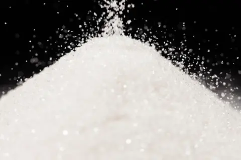 Biały, drobny proszek, przypominający cukier lub sorbitol, sypie się na stożek.