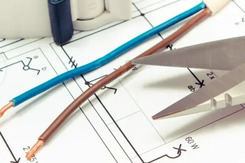 Niebieski i brązowy kabel, gotowe do cięcia, leżą na schemacie elektrycznym.