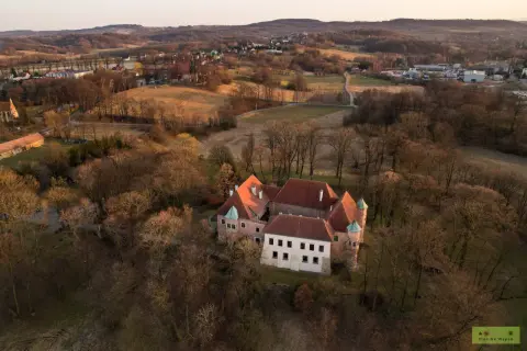Zamek w Dębnie otoczony drzewami, w tle pagórkowaty krajobraz o zachodzie słońca.