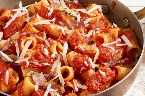 Rigatoni all'amatriciana dans une poêle en cuivre, garni de copeaux de parmesan. Un plat réconfortant et savoureux.