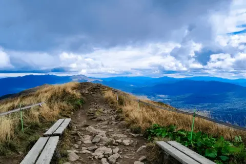 Kamienista ścieżka prowadzi na szczyt, skąd roztacza się widok na Bieszczady. W oddali widać kolejne pasma górskie.