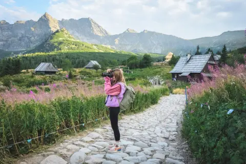 Dziewczynka z aparatem na tle górskich chat i kwitnących łubinów. Idealne miejsce na praktyczne kursy fotograficzne online.
