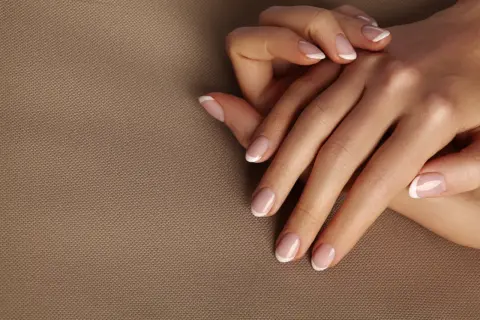 Dłonie z idealnym frenczem, podkreślającym naturalne kolory paznokci. Delikatny manicure na beżowym tle.