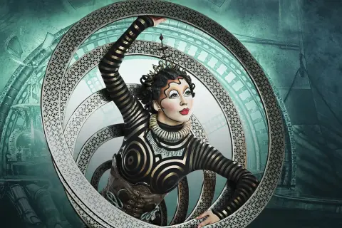 Artista del circo del sol en Zaragoza, con un traje de rayas doradas y negras, dentro de un aro metálico con intrincados diseños.