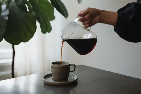 En hand häller upp mörkt kaffe ur en glaskanna i en mugg. Kaffet innehåller njutning och energi.