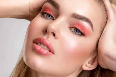 Viso di donna con ombretto corallo e un delicato blush o fard sulle guance.