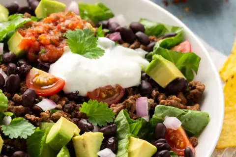 Ein bunter Taco Salat mit Hackfleisch, schwarzen Bohnen, Avocado, Tomaten, Zwiebeln und einem Klecks Sauerrahm. Perfekt für einen leichten Genuss.