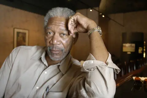 Morgan Freeman młody, z siwą brodą i zmarszczkami, opiera głowę na dłoni.