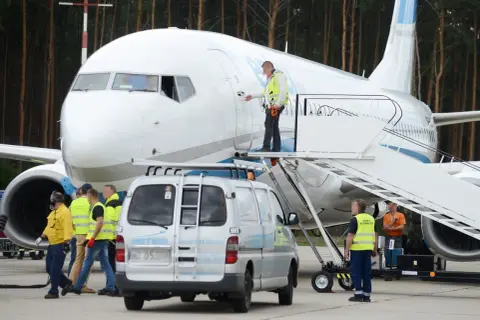 Pracownicy lotniska przygotowują samolot do lotów z Babimostu. Widać schody, furgonetkę i personel w kamizelkach odblaskowych.