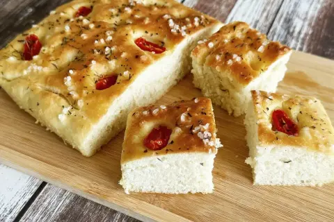 Puszysta, oryginalna włoska focaccia przepis z pomidorkami i solą morską, pokrojona na kawałki, gotowa do degustacji.