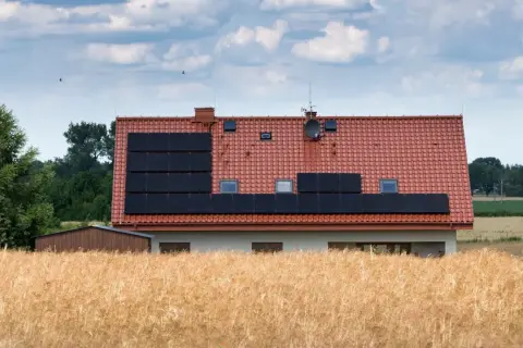 Dom z panelami słonecznymi na dachu, otoczony polami. Może to być znak, że nawet w spokojnej okolicy zdarzają się problemy z za wysokie napięcie w sieci.