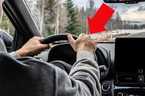 Förarens händer på ratten, en röd pil pekar mot vägen där det kan finnas vibrationer i bilen.