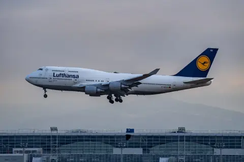 Lufthansa Boeing 747 im Landeanflug über einem modernen Flughafengebäude.