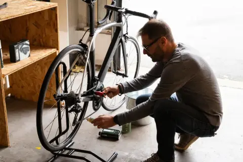 Mężczyzna przy rowerze wykonuje wymianę suportu, używając narzędzi i smaru.