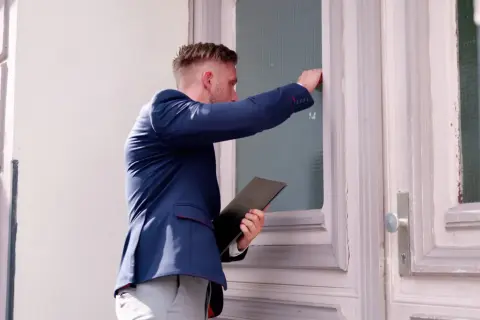 Mężczyzna w garniturze puka do drzwi, trzymając teczkę. Czy to komornik? Zastanawiasz się, ile może zabrać komornik?