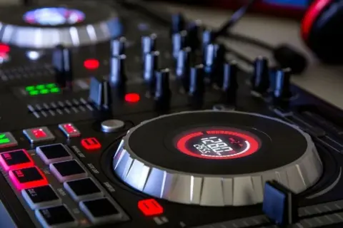 Zbliżenie na konsolę DJ-ską z podświetlanymi przyciskami i wyświetlaczem.