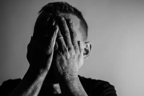Mężczyzna zakrywa twarz dłońmi, co może symbolizować przytłoczenie i zmęczenie, jedne z objawów neurastenii.