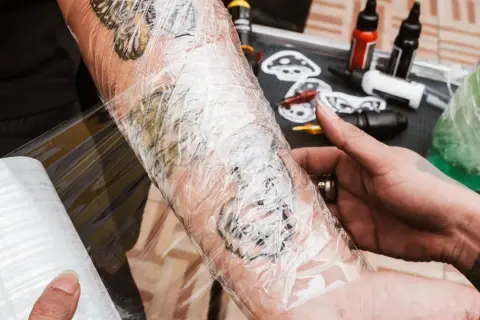 Frisch gestochenes Tattoo wird mit Tattoo-Folie geschützt. Die Folie schmiegt sich eng an, sodass keine Luft darunter ist.