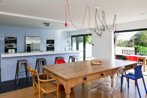 Un affascinante abbinamento sedie Kartell con tavolo antico in legno, circondato da una cucina moderna e un giardino lussureggiante.