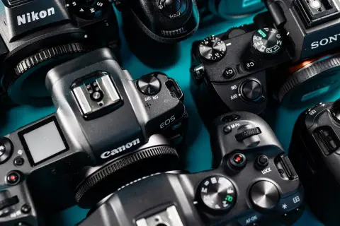 Zbliżenie na kilka aparatów fotograficznych marek Nikon, Canon i Sony, ułożonych na niebieskim tle.