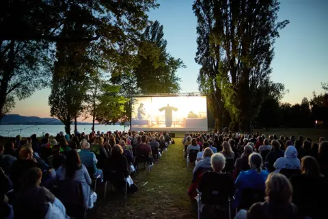 Open-air Kino in Boxberg: Viele Menschen sitzen auf Stühlen und schauen einen Film auf einer großen Leinwand am Seeufer.