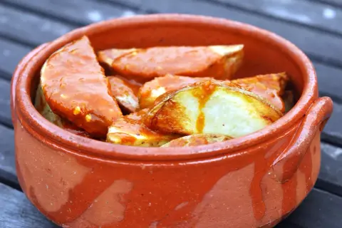 Patatas bravas, pommes de terre croustillantes nappées d'une sauce épicée, servies dans un plat en terre cuite.