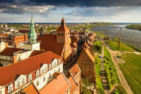 Widok na zabytki w Polsce: ceglane kamienice, kościół z zieloną wieżą i Wisła.