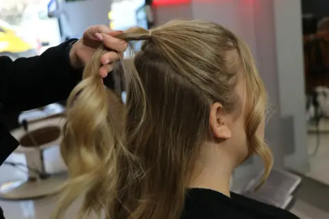 Tworzenie fryzury na Dzień Kobiet. Dłoń modeluje blond włosy, przygotowując je do stylizacji.