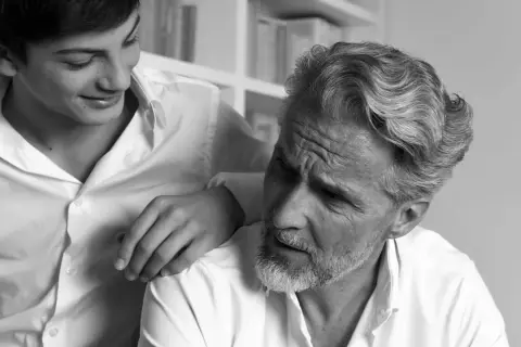 Un jeune homme pose sa main sur l'épaule d'un homme plus âgé, dont la barbe poil blanc est visible.