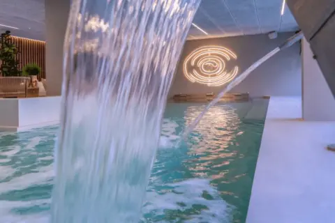 Cascada de agua en piscina interior, con iluminación circular y zona de descanso. Un oasis de spa sol y mar en Calpe.