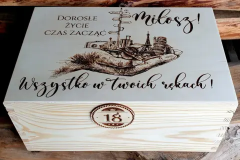 Drewniana skrzynka z grawerem: dłonie, walizki, wieże, drogowskazy, napis "Miłosz!" i "Wszystko w Twoich rękach!".