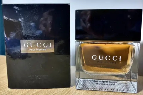 Elegancki zestaw z wodą po goleniu Gucci Pour Homme. Złocisty płyn w szklanym flakonie i czarne opakowanie.