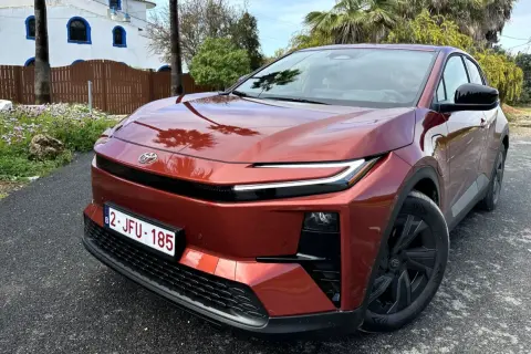 Nowa Toyota w kolorze miedzianym, zaparkowana przed białym budynkiem z niebieskimi oknami.