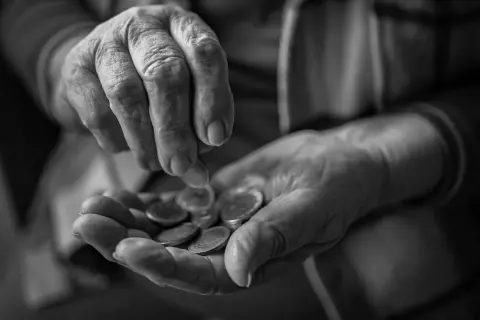 Mani anziane contano monete, un gesto che evoca la domanda su a quanto ammonta l'assegno di accompagnamento.