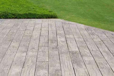 Pavimentazione marciapiede in cemento stampato effetto legno, adiacente a un prato verde ben curato.