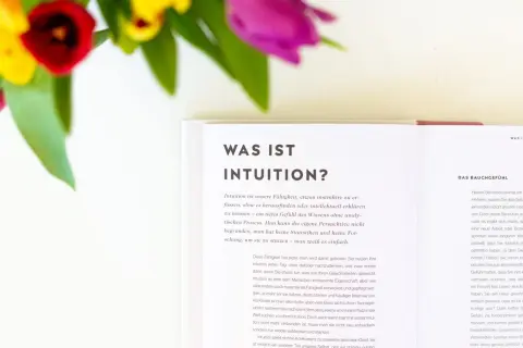 Blumen und ein Buch über Intuition. Lerne, deine Intuition zu trainieren und dem Bauchgefühl zu vertrauen.