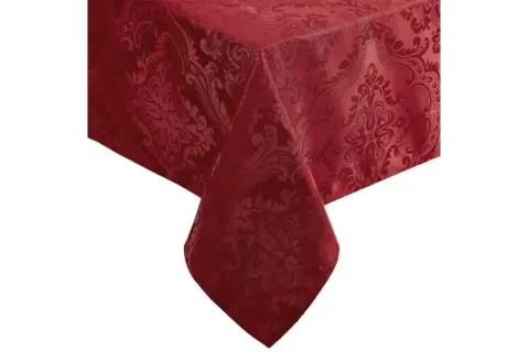 Un coin d'une table recouverte de nappes damassées rouge profond, ornées de motifs floraux complexes.