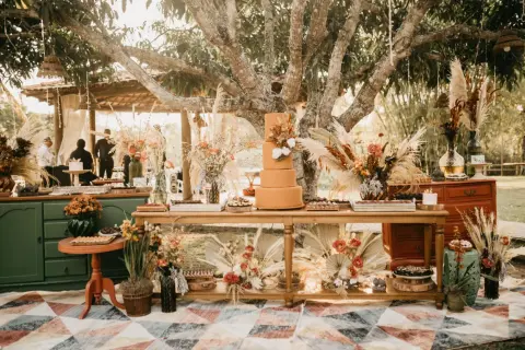 Un magnifique buffet de mariage thème automne, avec un gâteau orange, des fleurs séchées et des pampas sous un grand arbre.