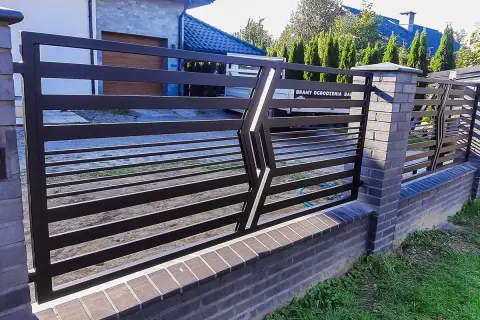 Nowoczesne, najładniejsze ogrodzenia kute z metalu, osadzone na ceglanym murku, tworzą elegancką barierę.