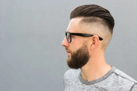 Mężczyzna z zarostem i modnym buzz cut, który sprytnie maskuje zakola.
