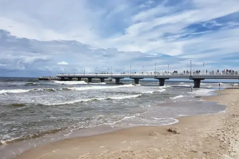 Kołobrzeg wczasy z wyżywieniem: spacer po molo, fale na plaży i tłumy turystów. Idealne miejsce na relaks nad Bałtykiem.