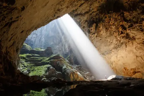 Promień słońca wpada do jaskini Son Doong, oświetlając zielone mchy i skalne tarasy.