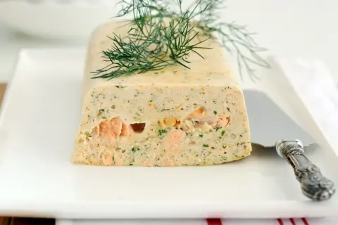 Elegancka terrina z łososia, ozdobiona gałązką koperku, prezentuje się apetycznie na białym talerzu.