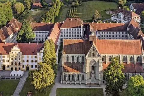Luftaufnahme eines beeindruckenden schloss im Bodenseekreis mit roten Ziegeldächern, umgeben von grünen Bäumen und gepflegten Gärten.