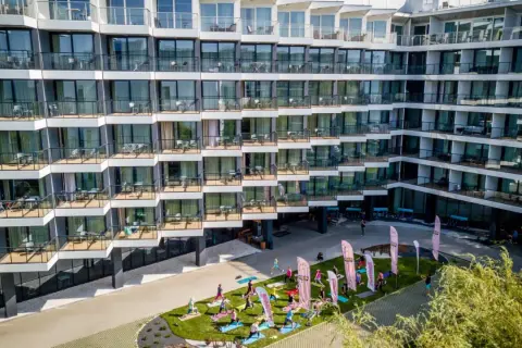 Grupa osób ćwiczy jogę na trawniku przed nowoczesnym seaside park hotel.