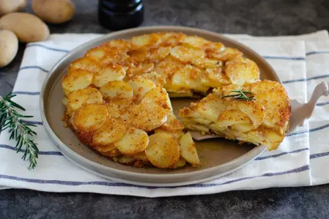 Un delizioso tortino di patate dorato e croccante, servito su un piatto con rosmarino fresco.