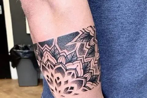 Eleganckie tatuaże męskie na ramieniu w stylu mandali, z motywami liści i geometrycznymi wzorami, wykonane techniką dotwork.