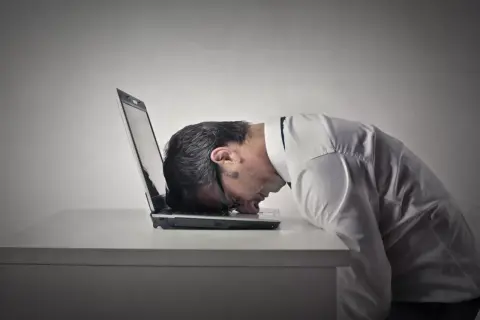 Zrezygnowany mężczyzna z głową na laptopie. Czas na naukę, jak zmienić negatywne myślenie na pozytywne.